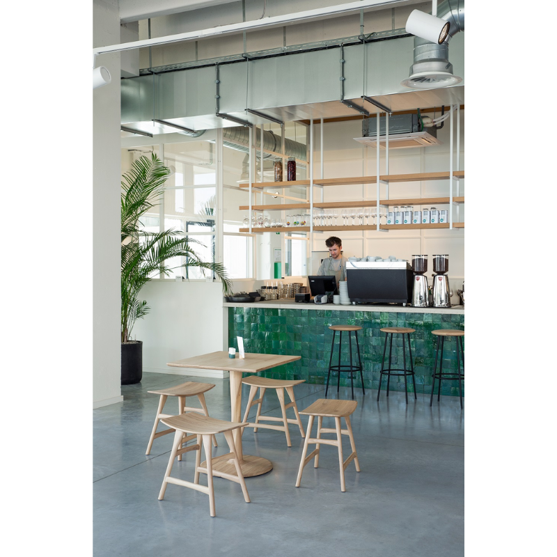 The Baretto Bar Stool from Ethnicraft next to the bar in a professional coffee shop, showcasing the products functionality in cafes, restaurants and other commercial settings.