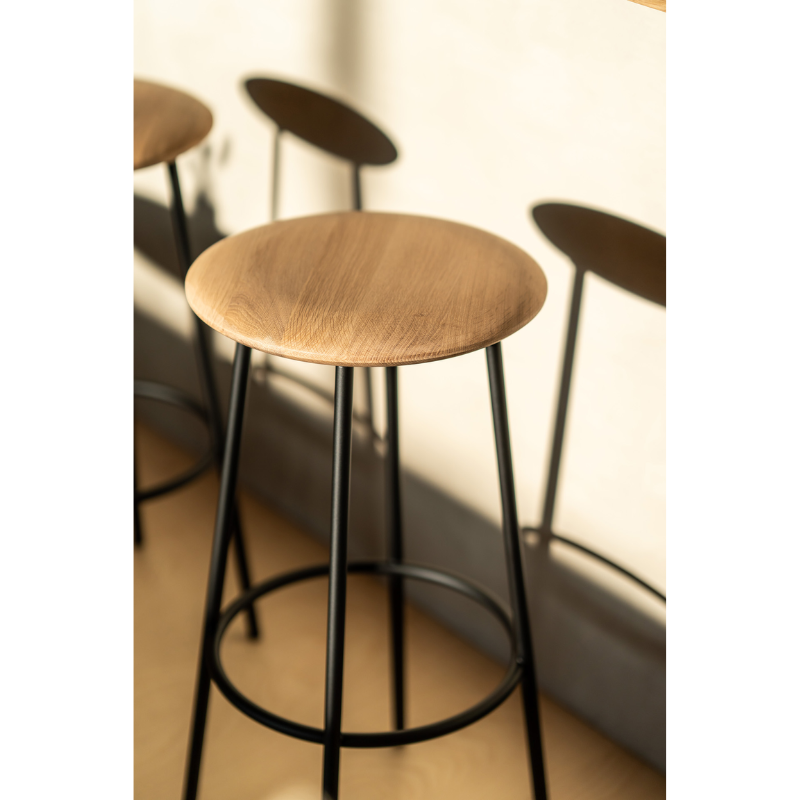 The Baretto Bar Stool from Ethnicraft in a living space, casting a shadow against the nearby bar.