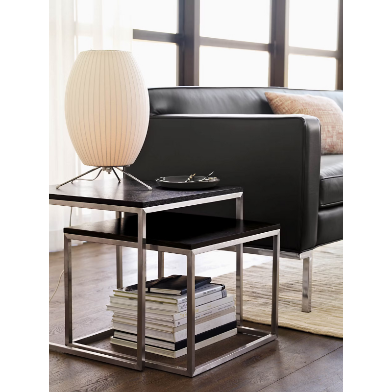 The Nelson Cigar Tripod Table Lamp from Herman Miller in a living room lifestyle photograph beside a couch.