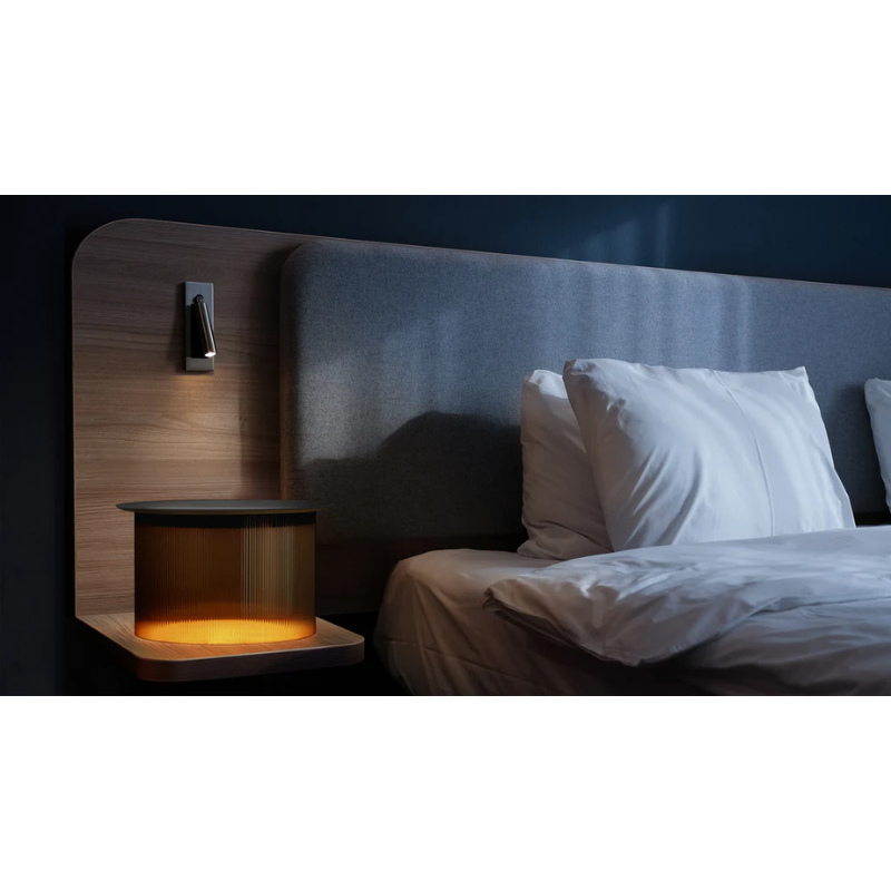 The large Carousel Table next a bed during the nighttime in a bedroom.