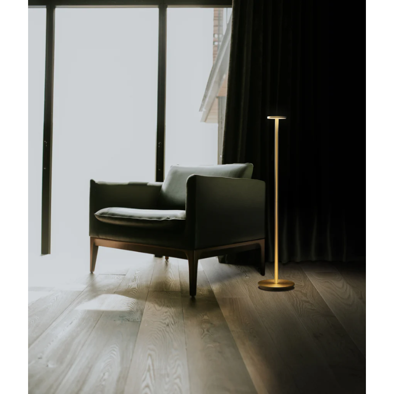 The portable light, Luci Floor from Pablo Designs within a living room next to a lounge chair.