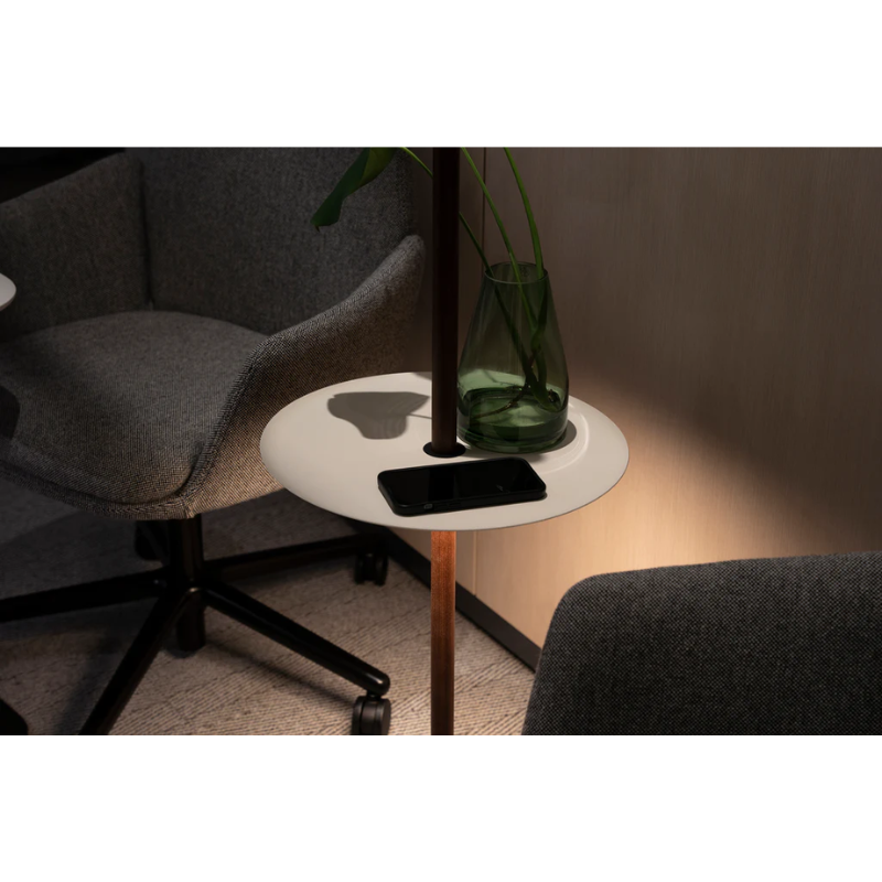 The Nivél Pedestal from Pablo Designs in a family area with a planter and phone on top, while the light illuminates the room.