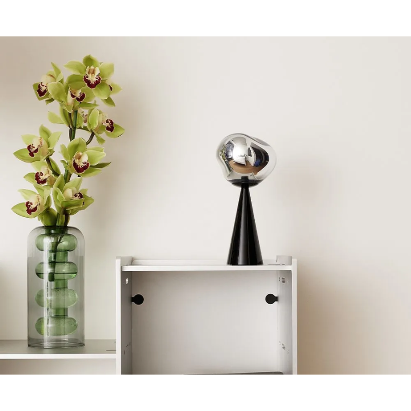 A Bump Vase Tall in Green by Tom Dixon on top of a bookshelf next to a portable LED.