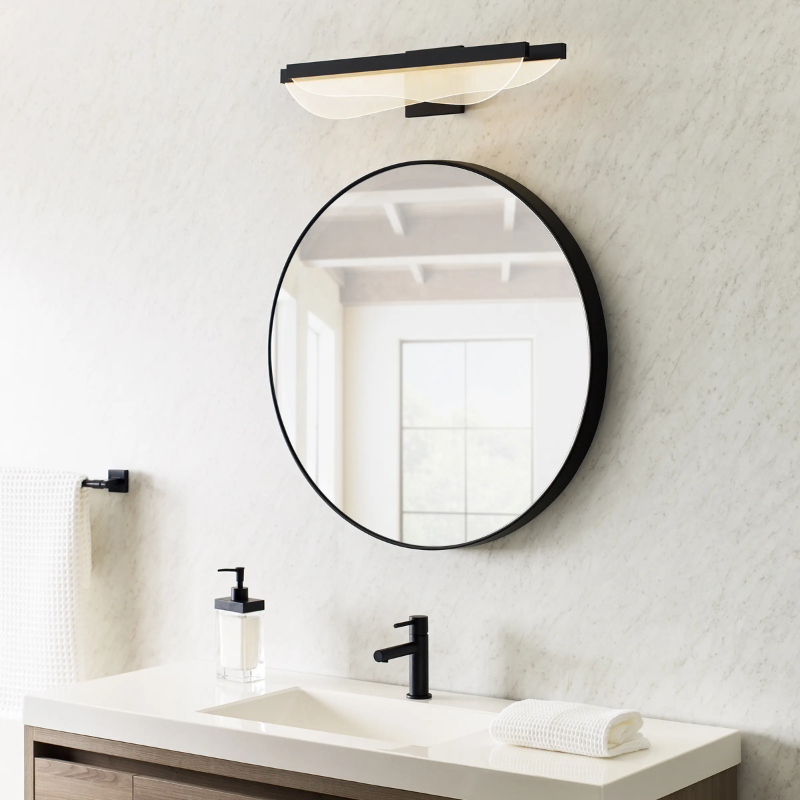 The Nyra Bathroom Sconce from Visual Comfort and Co above a sink and mirror in an angled shot.