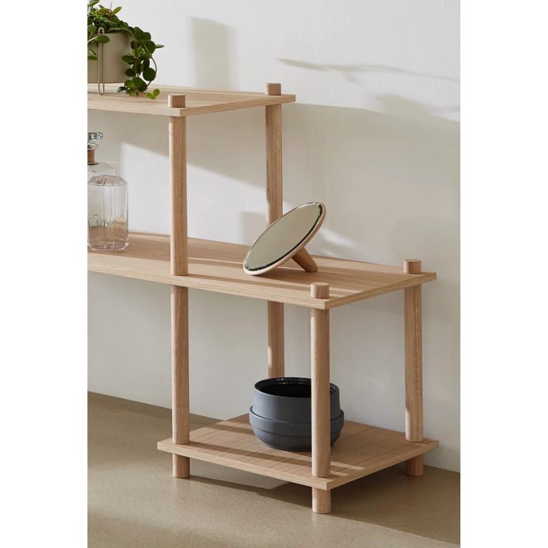 The Mirror Barb from Woud with handle, resting on top of a bookshelf in a living room.