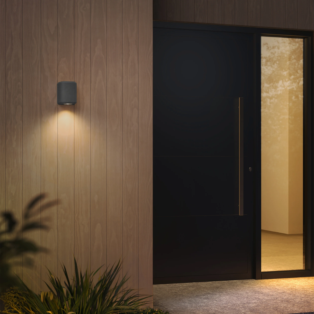 The Brixham Wall Single outdoor sconce in charcoal concrete by Astro Lighting installed by a front door at night.