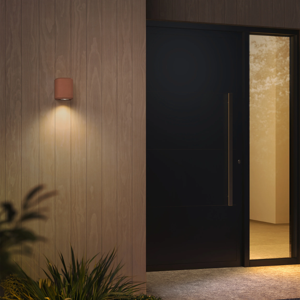The Brixham Wall Single outdoor sconce in terracotta concrete by Astro Lighting installed by a front door at night.