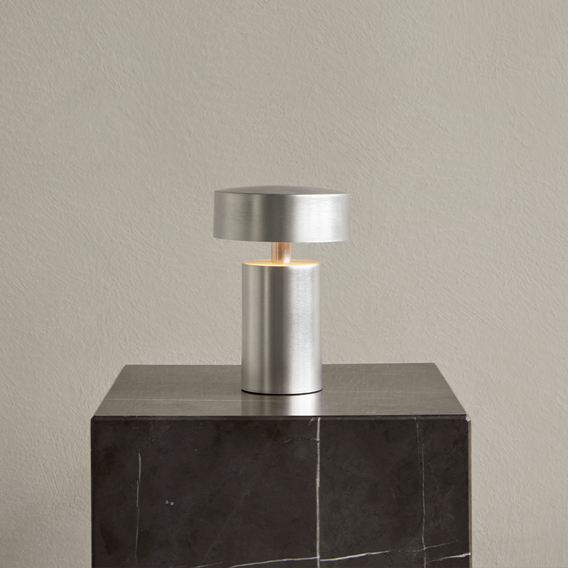 The Column Portable Table Lamp from Audo Copenhagen in brushed aluminum on a marble side table.