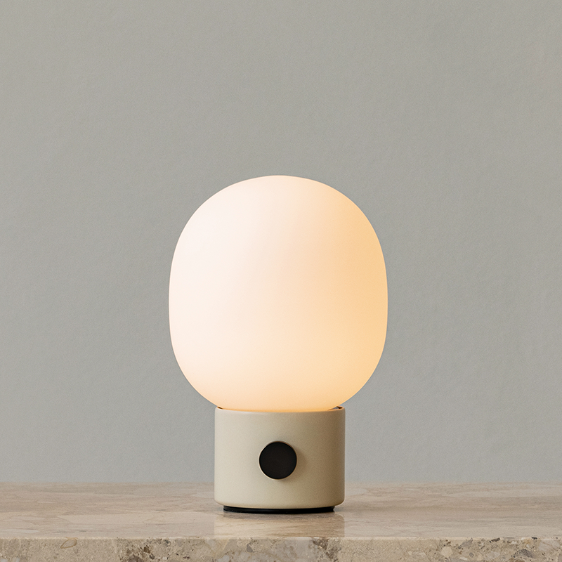 The JWDA Portable Table Lamp from Audo Copenhagen in alabaster white in a lounge with the light turned on.