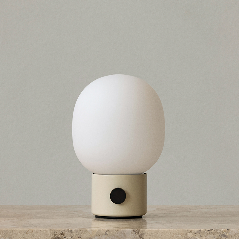 The JWDA Portable Table Lamp from Audo Copenhagen in alabaster white on a marble shelf.