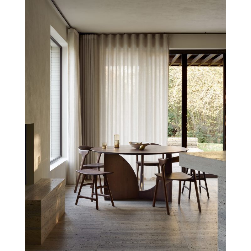 The brown teak Round Geometric Dining Table from Ethnicraft in a dining room.