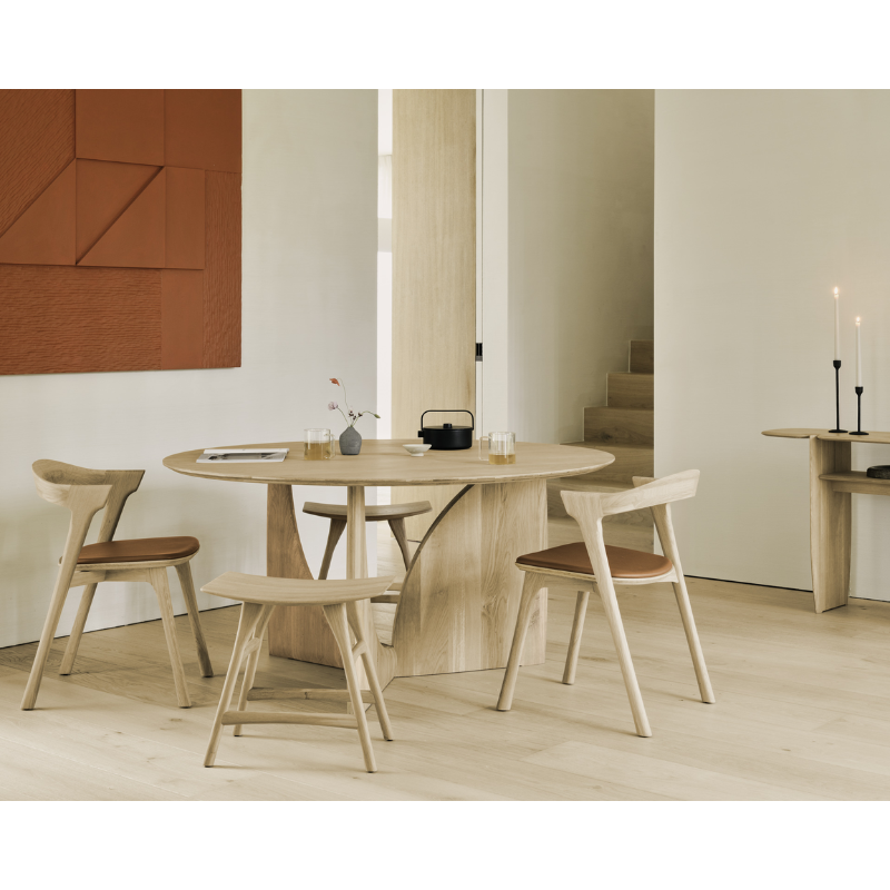 The oak Round Geometric Dining Table from Ethnicraft in a dining room with upholstered Bok Dining Chair and Osso Dining Stool.