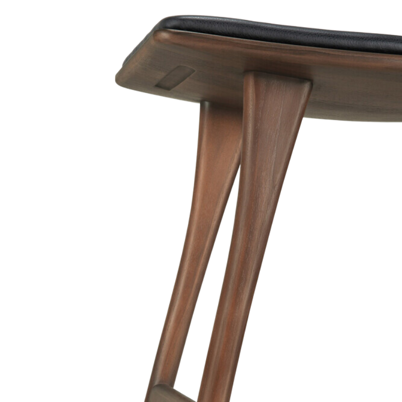 The Upholstered Osso Counter Stool from Ethnicraft with brown teak wood and black leather in detail.
