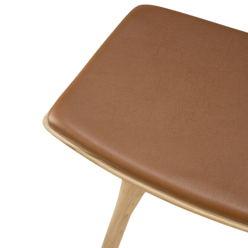 The Upholstered Osso Dining Stool from Ethnicraft with oak and cognac leather seat.