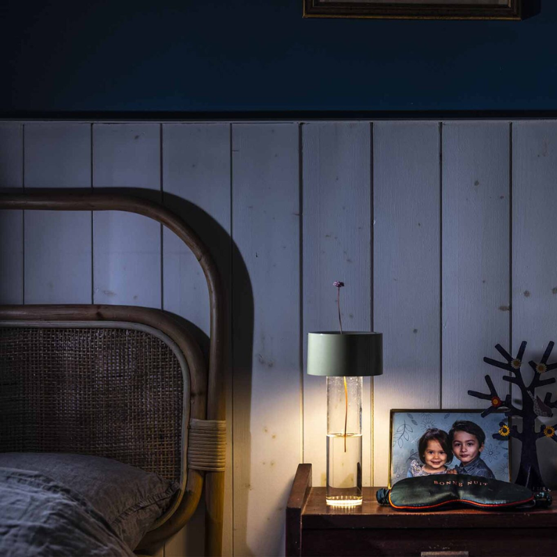 The Fleur Portable Lamp from Foscarini in sage green on a bedside table.