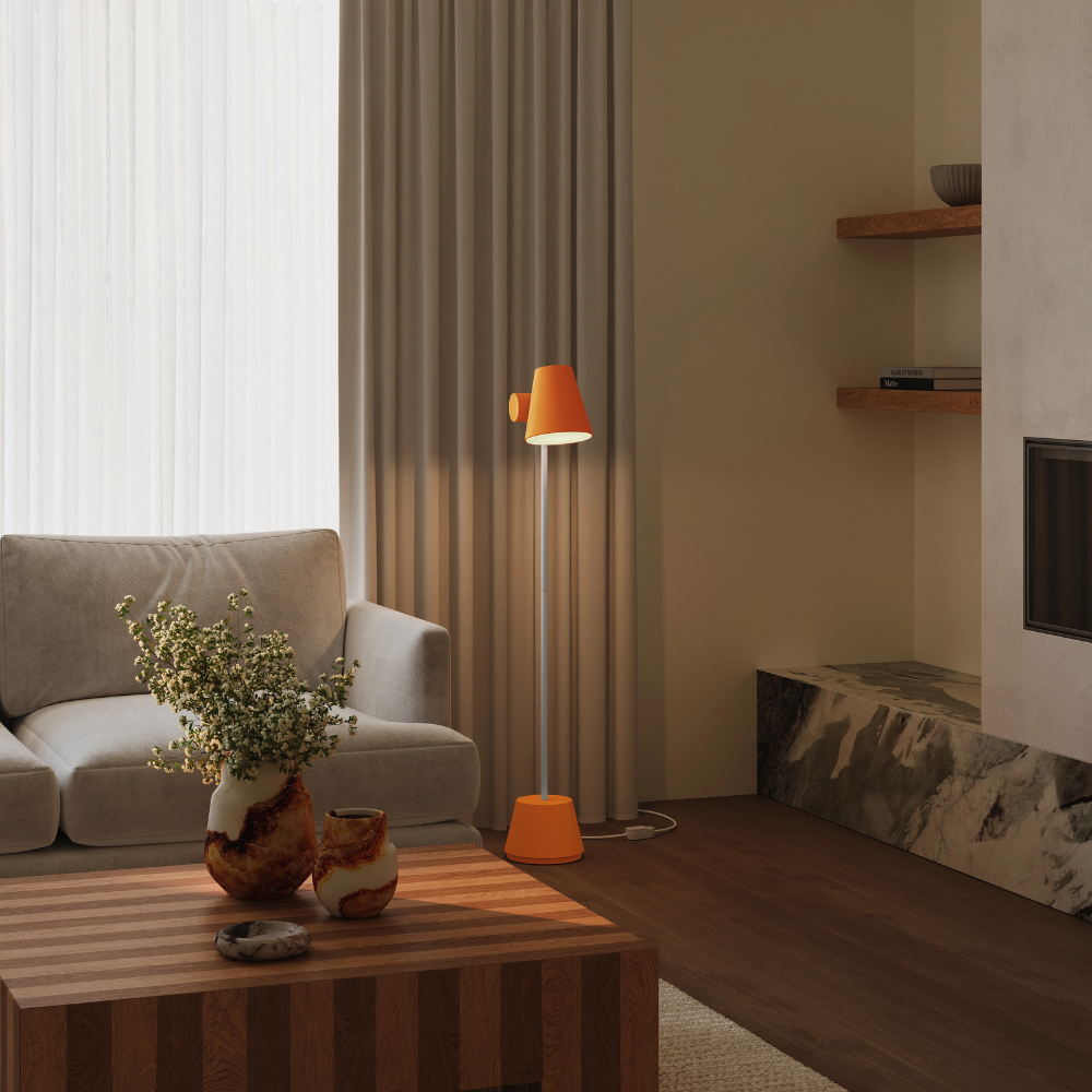 The persimmon Aim Floor Light from Gantri with the white rod option in a living room next to a couch.