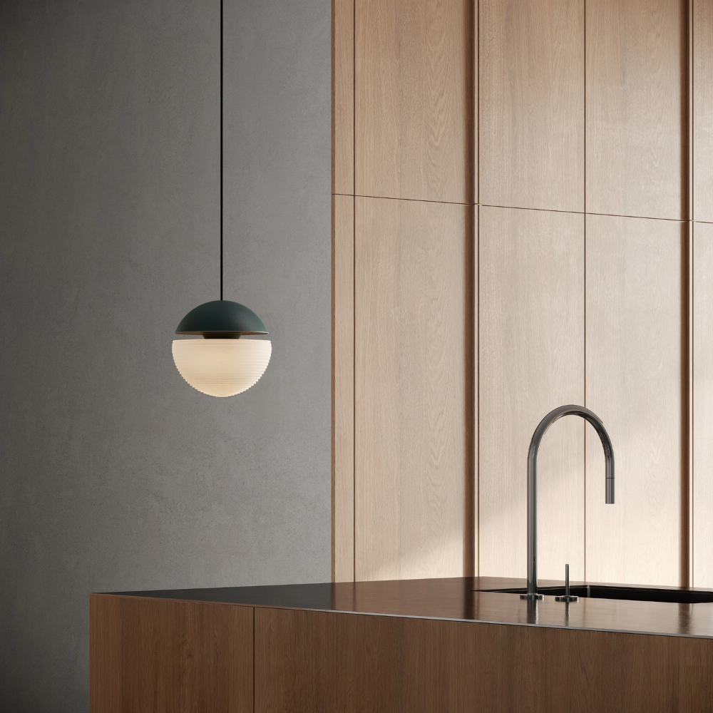 The forest Cora Pendant Light from Gantri with the black cord in a kitchen and dining area above an island with a sink.