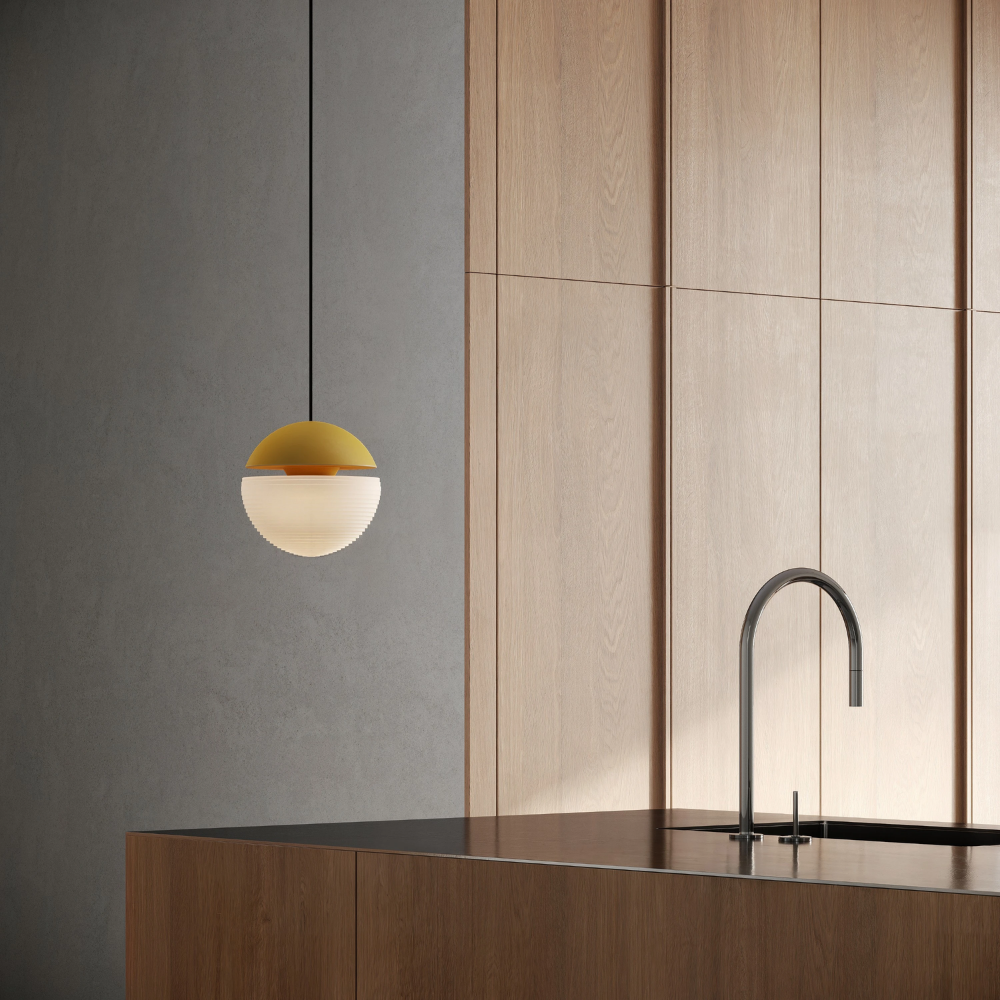 The mustard Cora Pendant Light from Gantri with the black cord in a kitchen and dining area above an island with a sink.