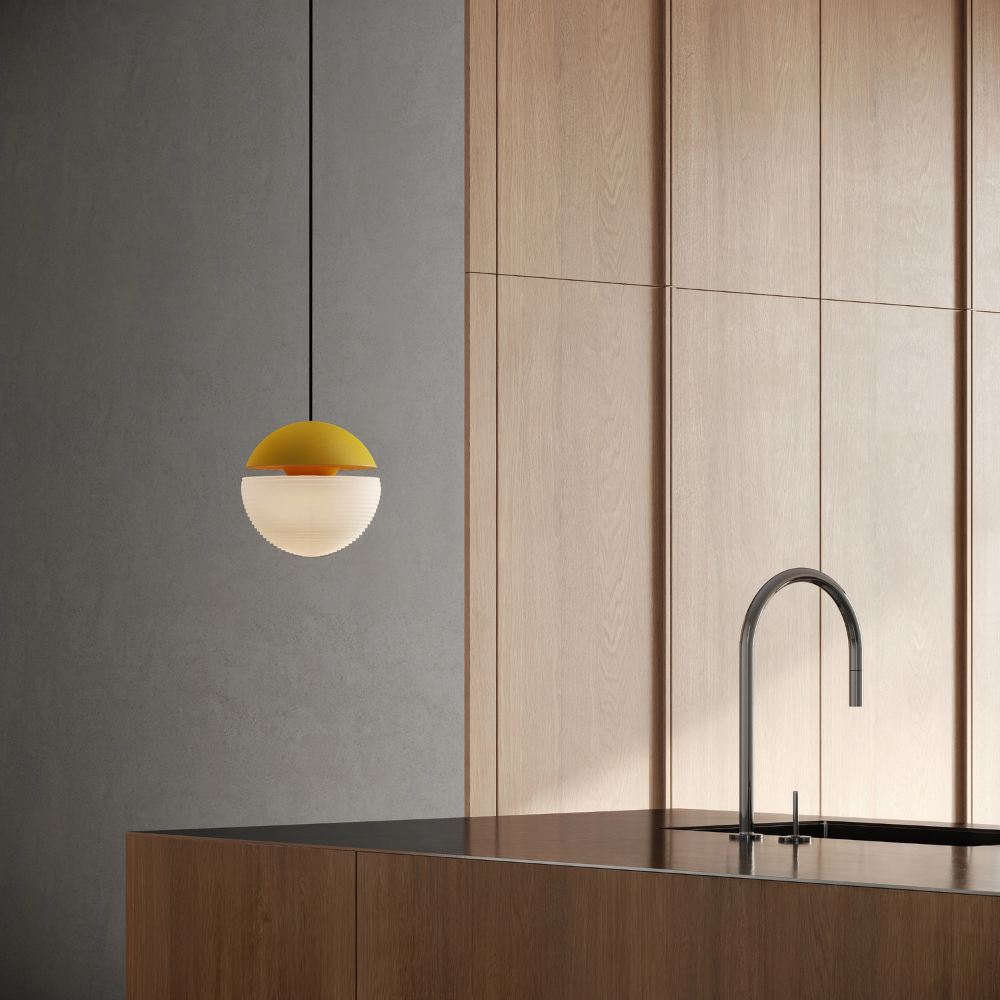 The sunrise Cora Pendant Light from Gantri with the black cord in a kitchen and dining area above an island with a sink.