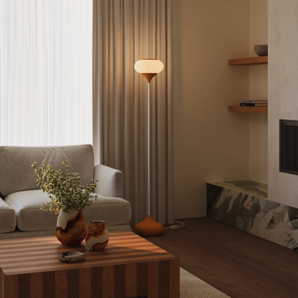 The persimmon Kobble Floor Light from Gantri with the white rod option in a lounge space next to a sofa.