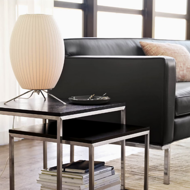 The Nelson Cigar Tripod Table Lamp from Herman Miller in a living room lifestyle photograph beside a couch.