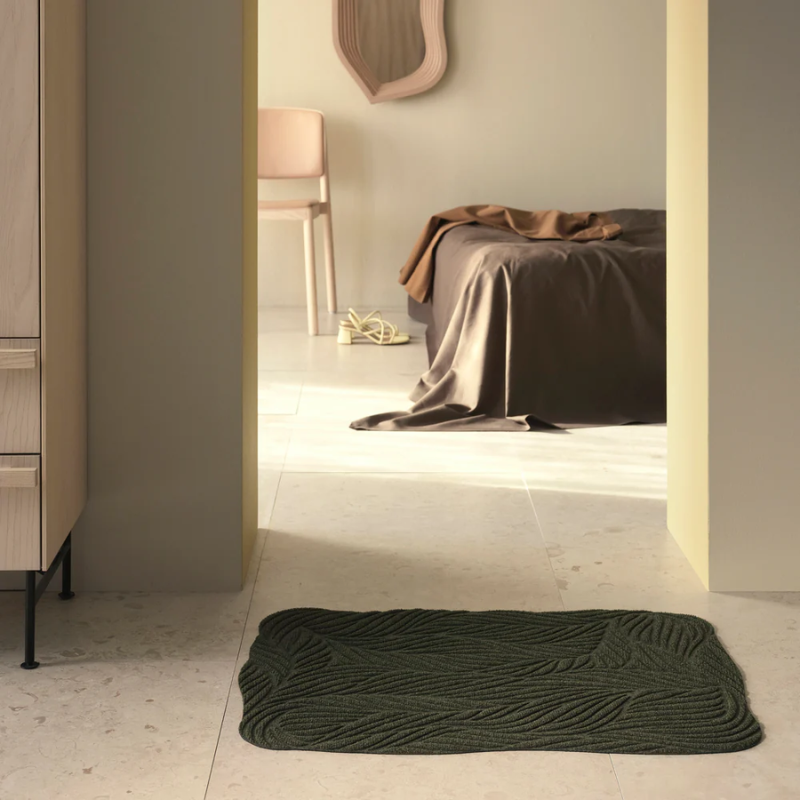 The Twine Doormat from Heymat in green in a bedroom.