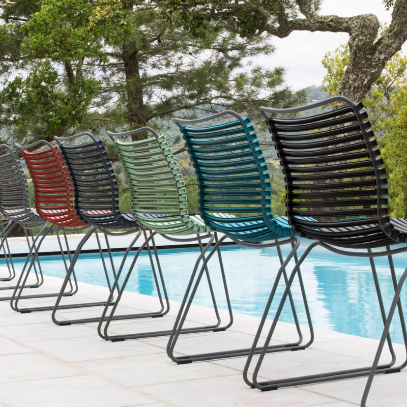 The Click Outdoor Dining Chair No Armrest by Houe is shown with multiple color options beside a pool.