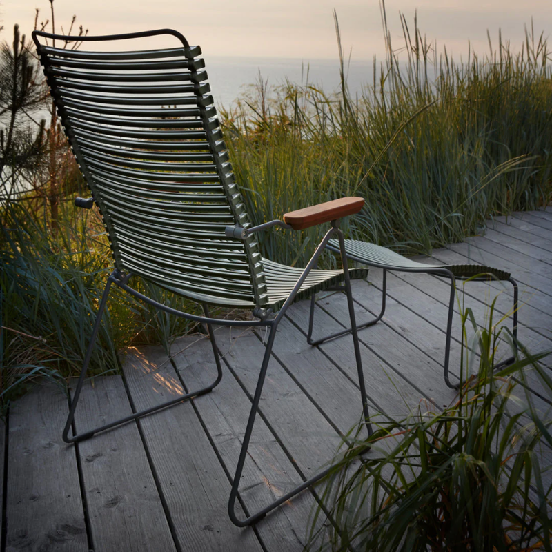 The Click Outdoor Footrest by Houe with a chair on a wooden deck with grass.