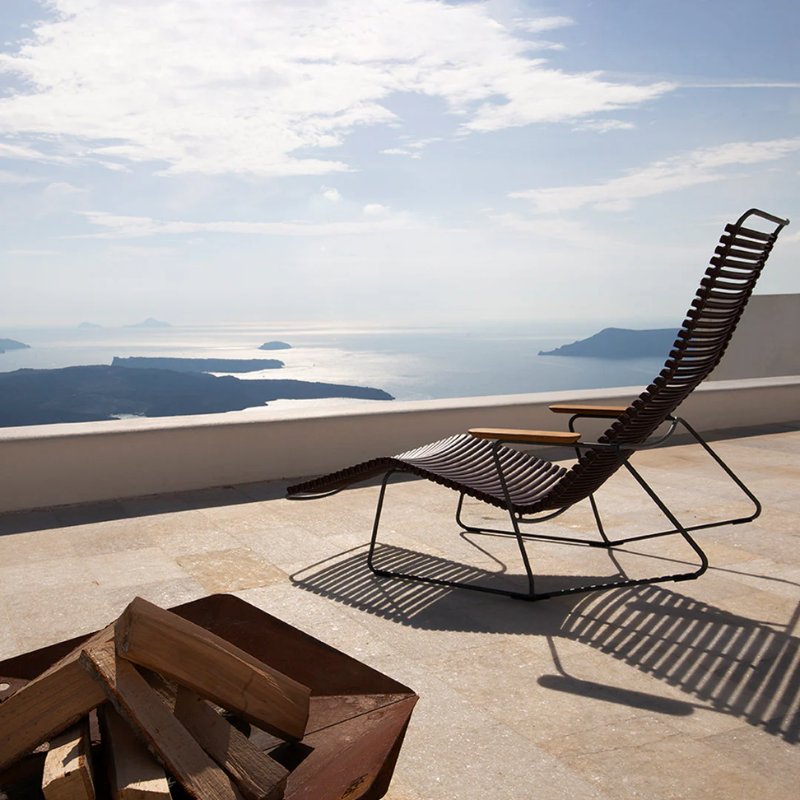 The Click Outdoor Sunrocker by Houe on a rooftop with a scenic view of the ocean and mountains.
