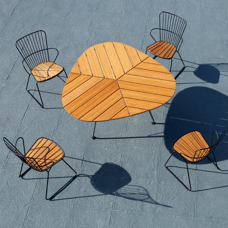 The Leaf Outdoor Dining Table by Houe with chairs on a textured gray surface from the top view.