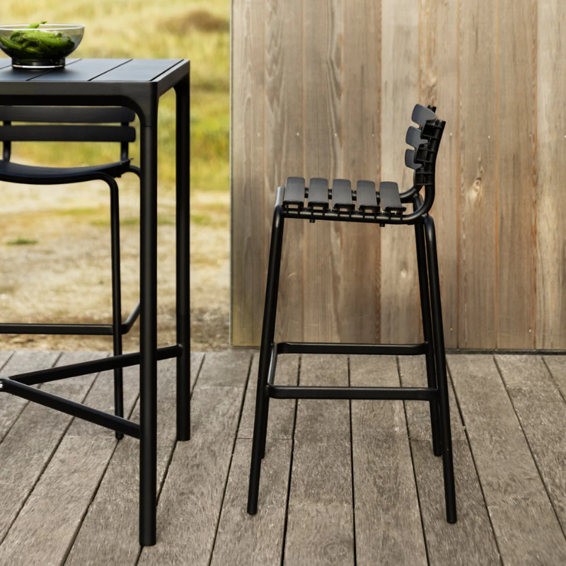 The ReClips Outdoor Bar Chair by Houe with a stool and a small table outdoors.