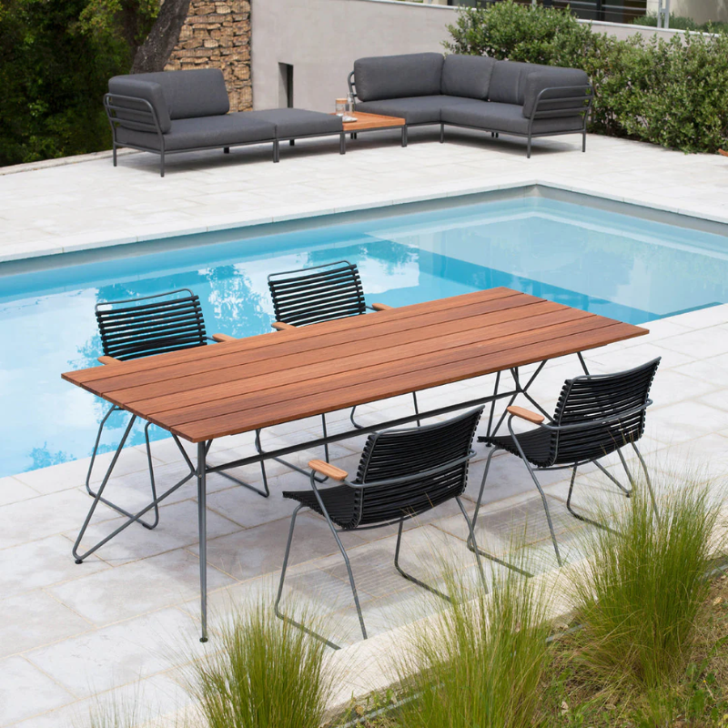 The Sketch Outdoor Dining Table from Houe with black chairs beside the pool.