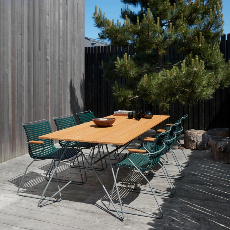 The Sketch Outdoor Dining Table from Houe with green chairs in the outdoor area.