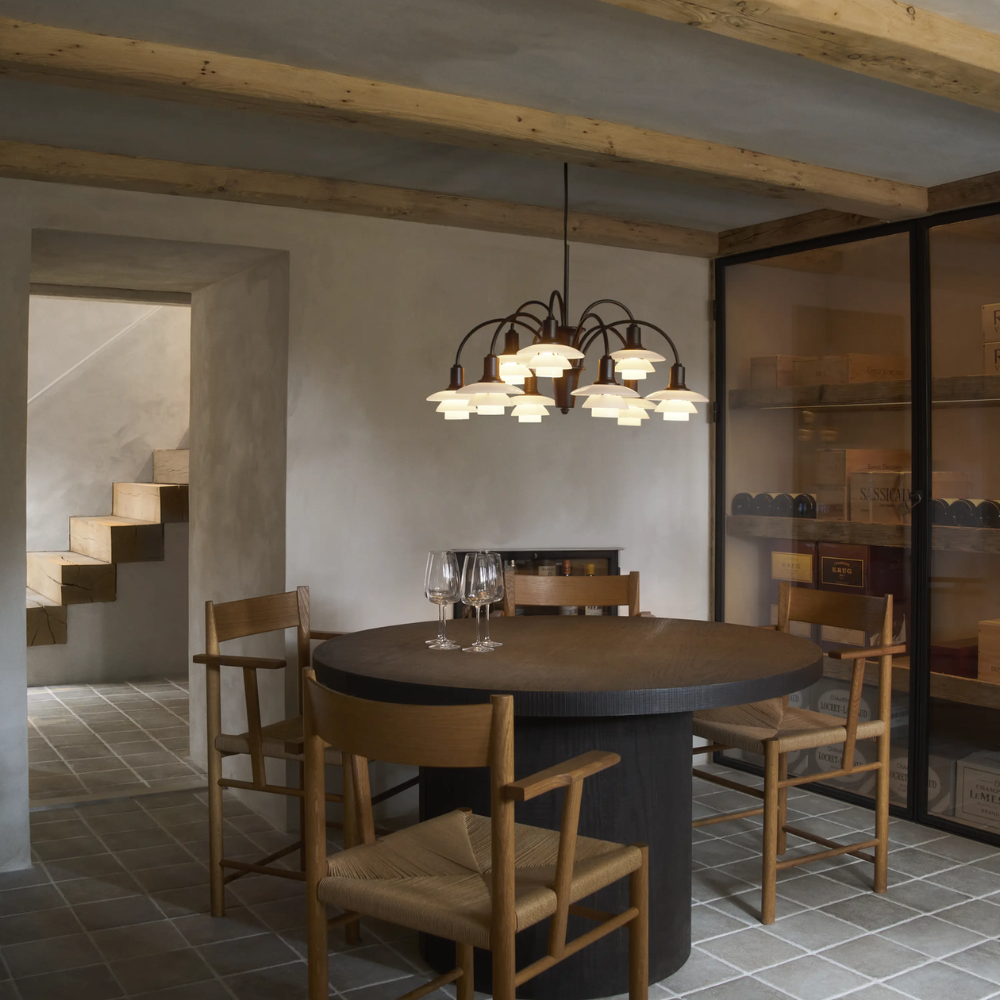 The PH 1/1 Chandelier, 9-Light by Louis Poulsen over a dining table turned on.