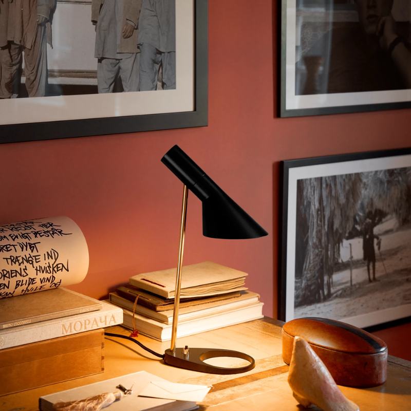 The AJ Mini Table Lamp in Brass/Black on a desk.