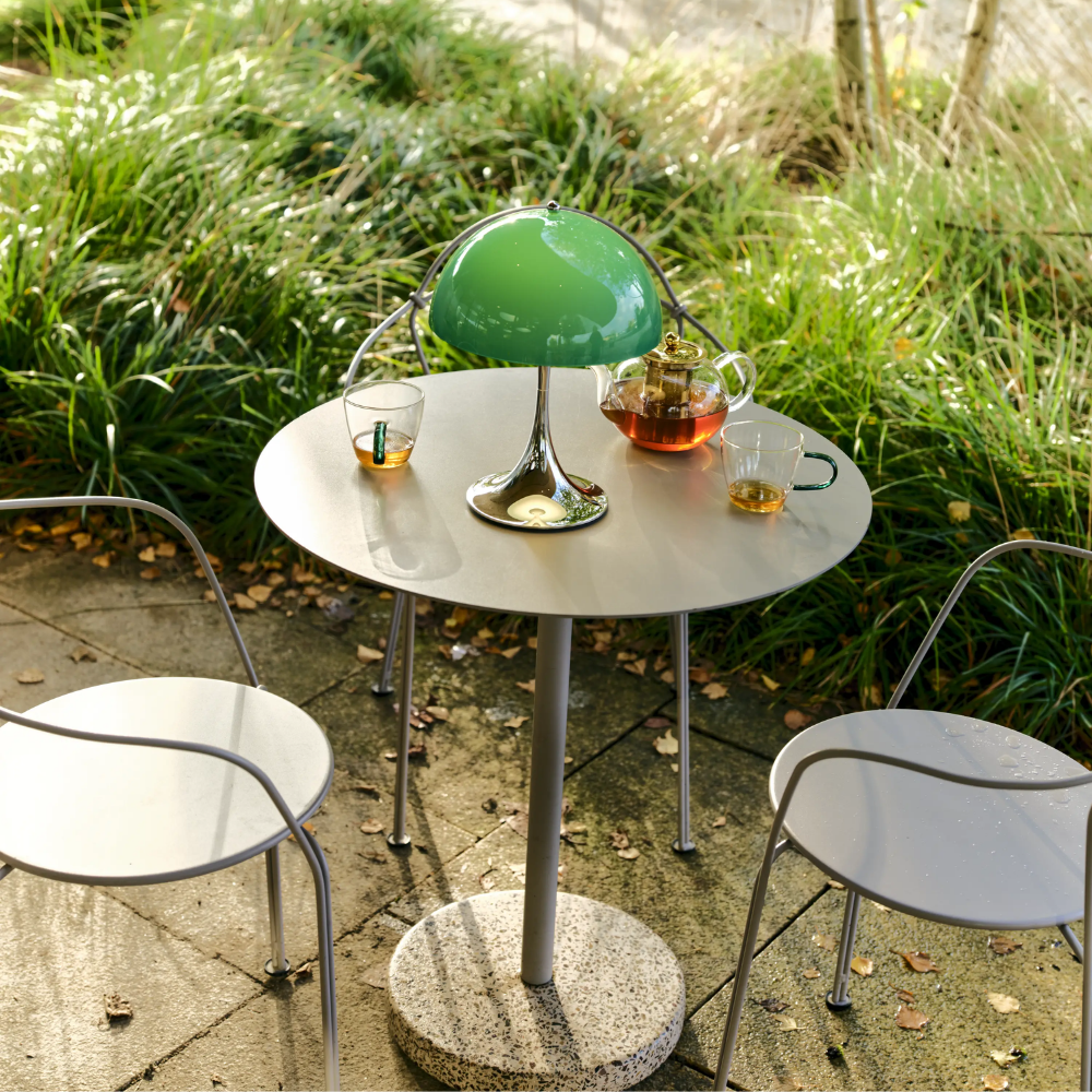 The Panthella 250 Portable Table Lamp from Louis Poulsen in Original Opal Green on an outdoor table turned on.