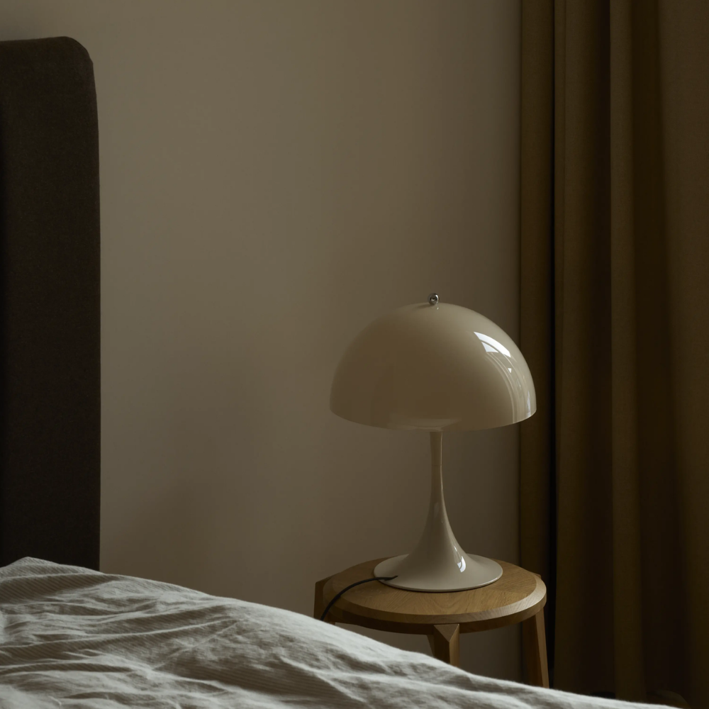 The Panthella 320 Table Lamp from Louis Poulsen in Opal Beige next to abed turned off.