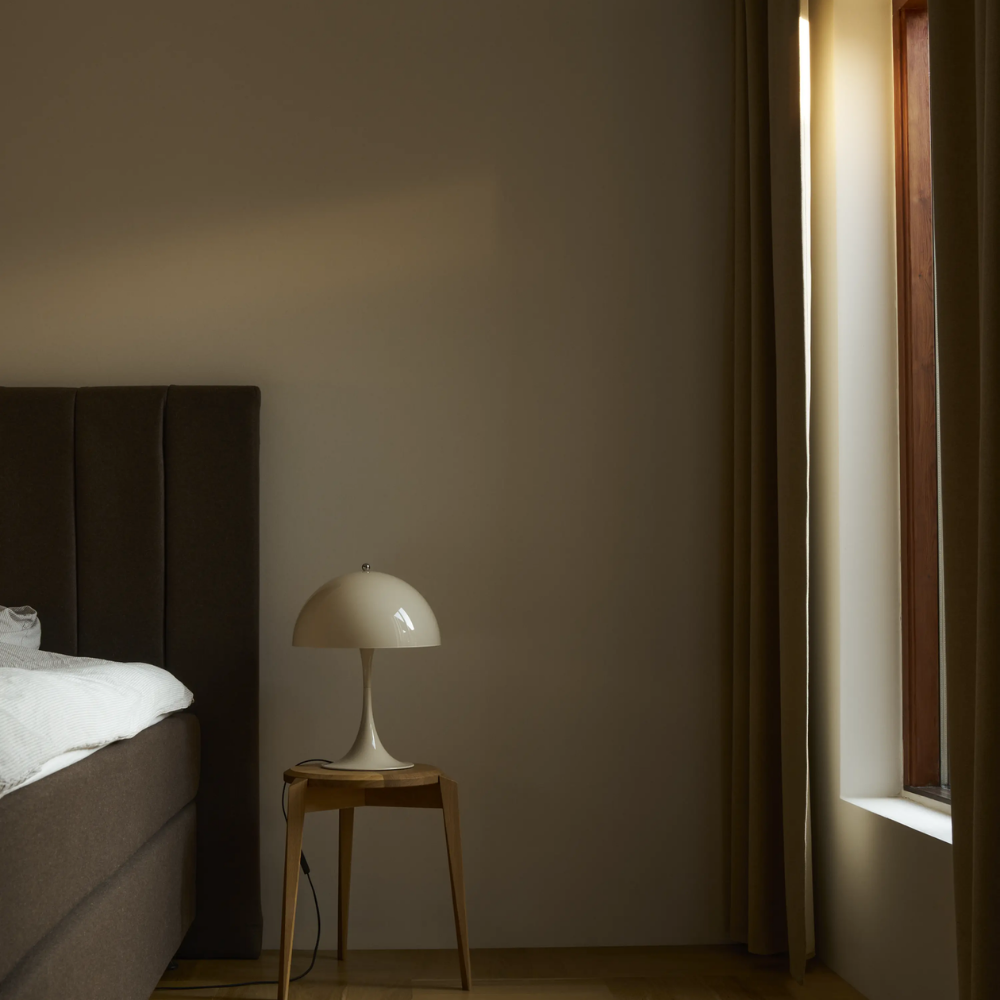 The Panthella 320 Table Lamp from Louis Poulsen in Opal Beige next to a bed.