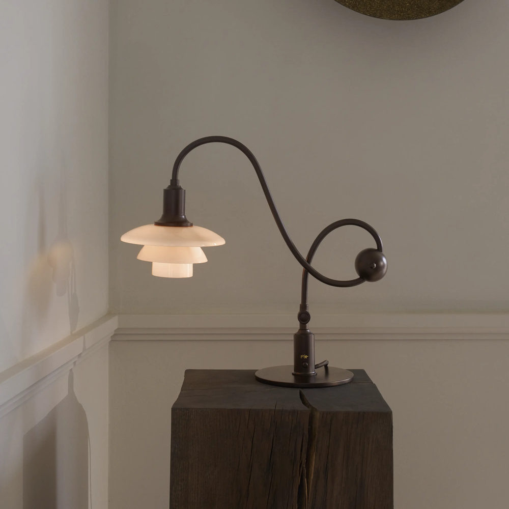 The PH 1/1 Piano Table Lamp by Louis Poulsen on a pedestal turned on.