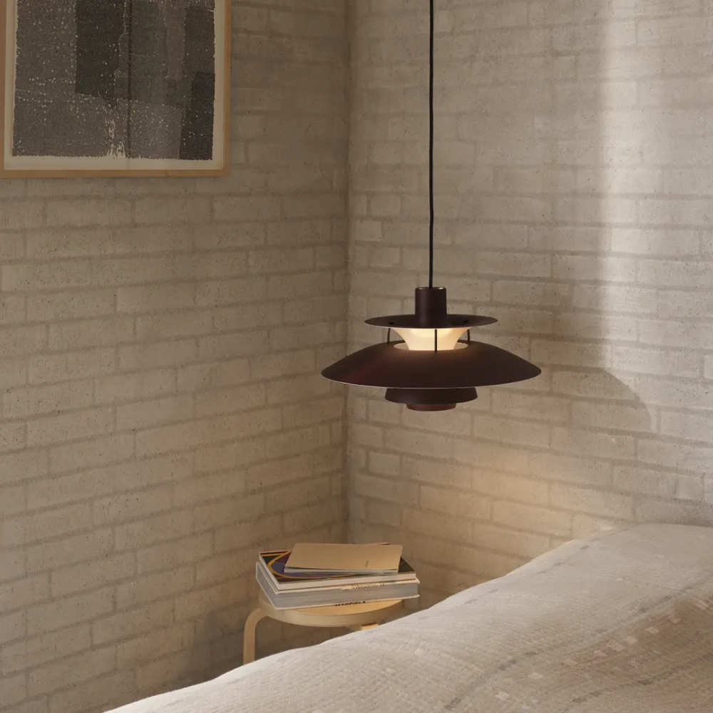 The PH 5 from Louis Poulsen in monochrome burgundy in a bedroom next to a bed.