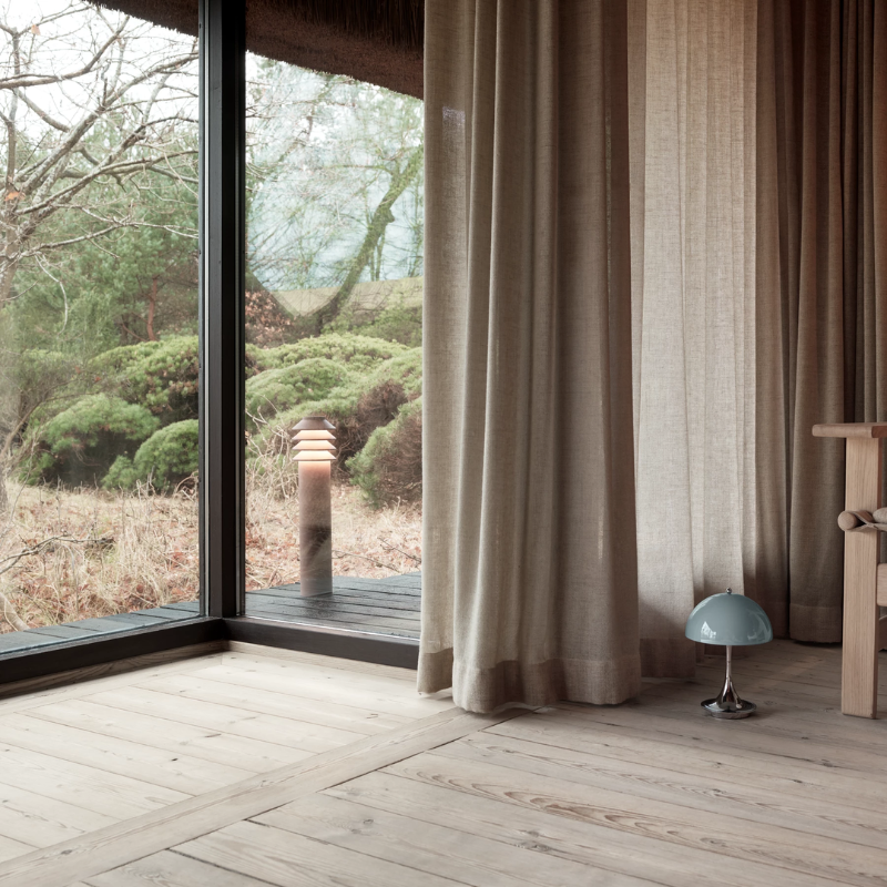 The Tall Bysted Garden Bollard from Louis Poulsen in corten in a garden outside a living room.