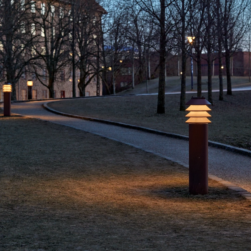 The Tall Bysted Garden Bollard from Louis Poulsen in corten beside a pathway.