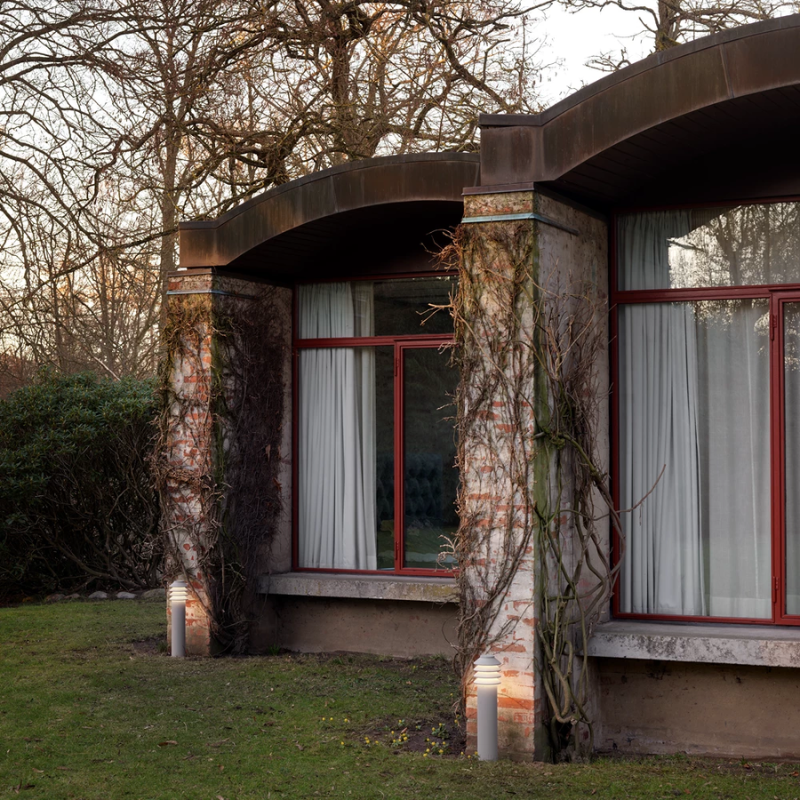 The Tall Bysted Garden Bollard from Louis Poulsen in natural paint aluminum outside a home.