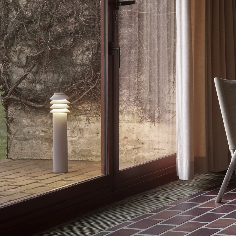 The Tall Bysted Garden Bollard from Louis Poulsen in natural paint aluminum outside a living space.