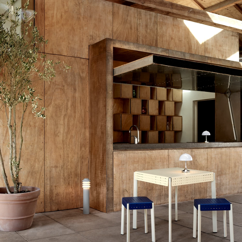 The Tall Bysted Garden Bollard from Louis Poulsen in natural paint aluminum in an outdoor dining area.