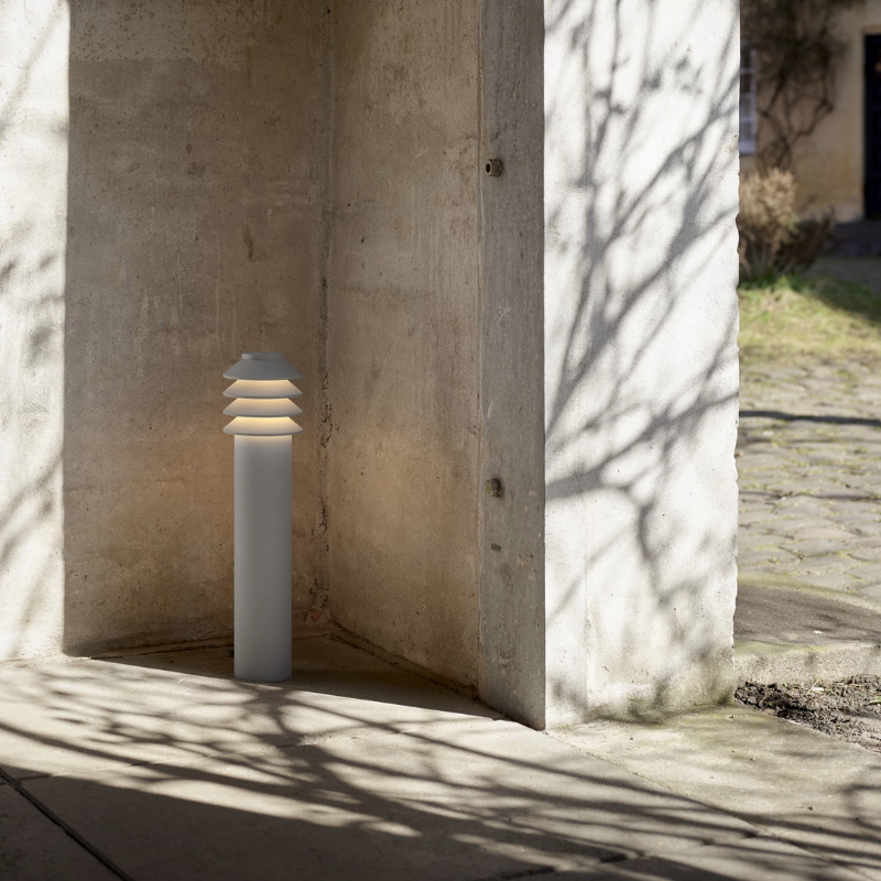 The Tall Bysted Garden Bollard from Louis Poulsen in natural paint aluminum by an outdoor path.