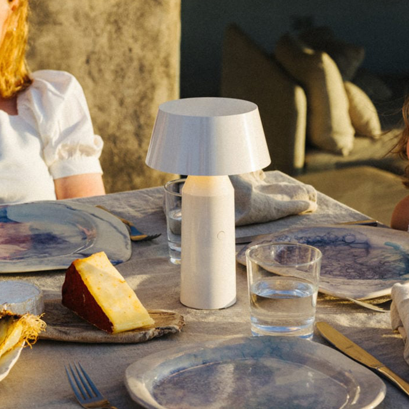 The Bicoca Portable Table Lamp from Marset in off-white in a outdoor dining space.
