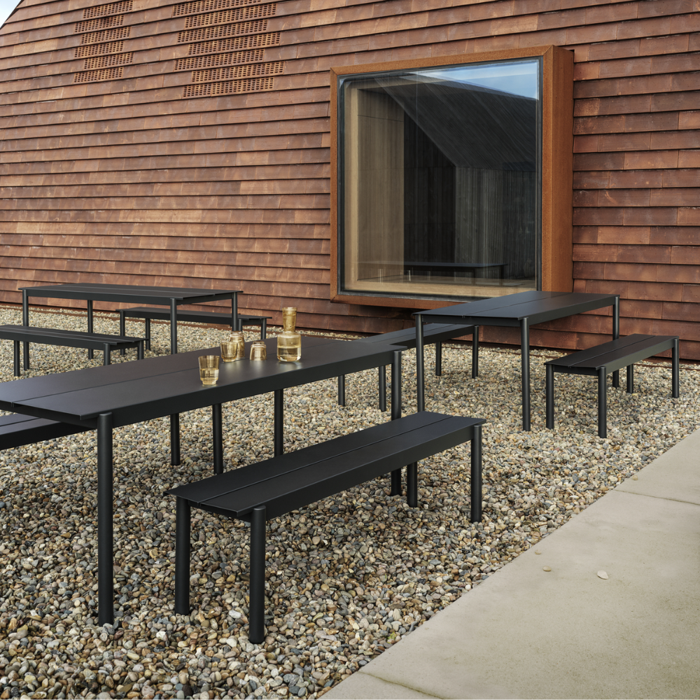 The black Linear Steel Bench from Muuto in a cafe garden.