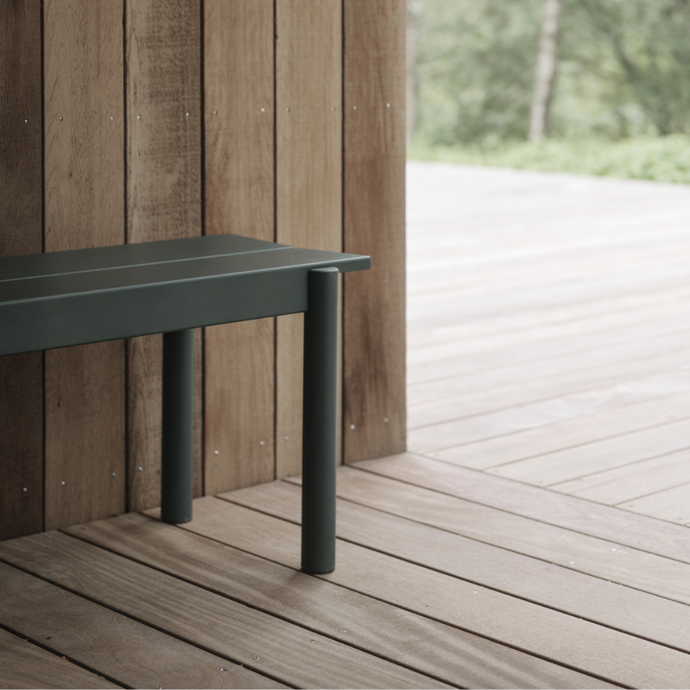 The dark green Linear Steel Bench from Muuto in an outdoor living area.