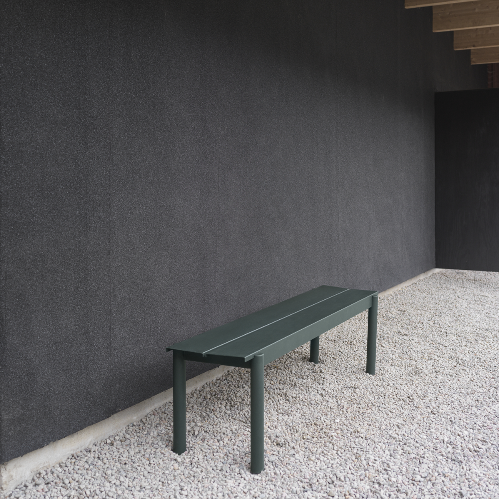 The dark green Linear Steel Bench from Muuto in an outdoor living space.